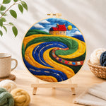 Finished abstract swirling fields and red roof cottage needle felting displayed on a wooden easel