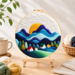 Finished abstract wavy mountains and tiny houses needle felting displayed on a wooden easel