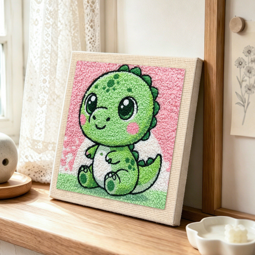 Baby green dinosaur with big eyes punch needle artwork displayed on a table