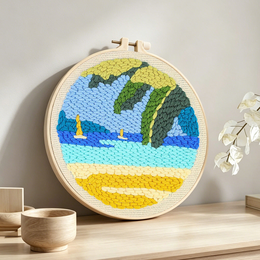 Beach with sailboats and tropical leaves punch needle artwork displayed on a table