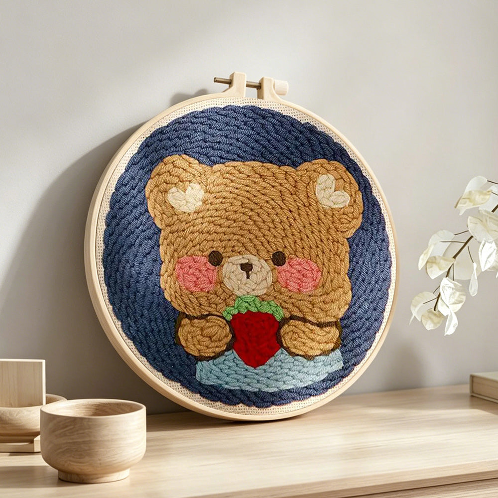 Bear holding strawberry punch needle artwork displayed on a table