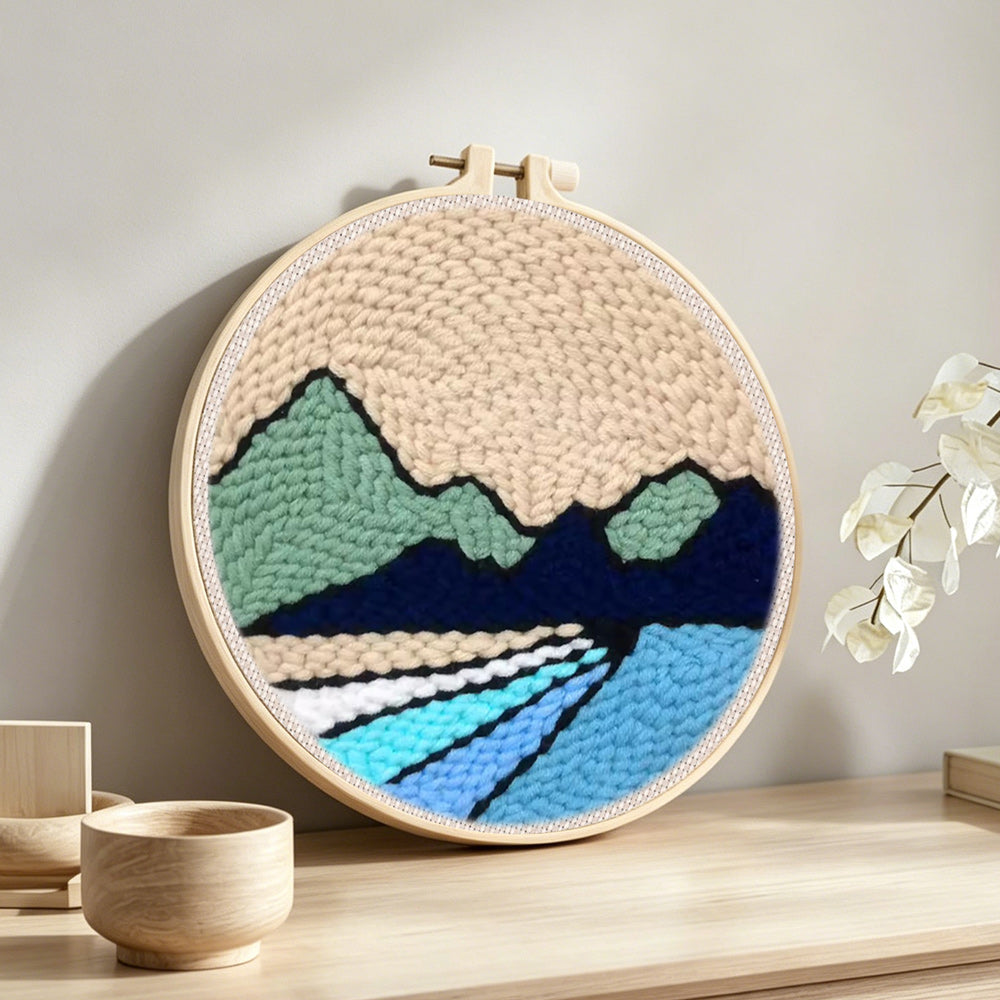 Beige sky, green hills and blue rivers punch needle artwork displayed on a table