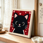 Big-eyed black cat face punch needle artwork displayed on a table