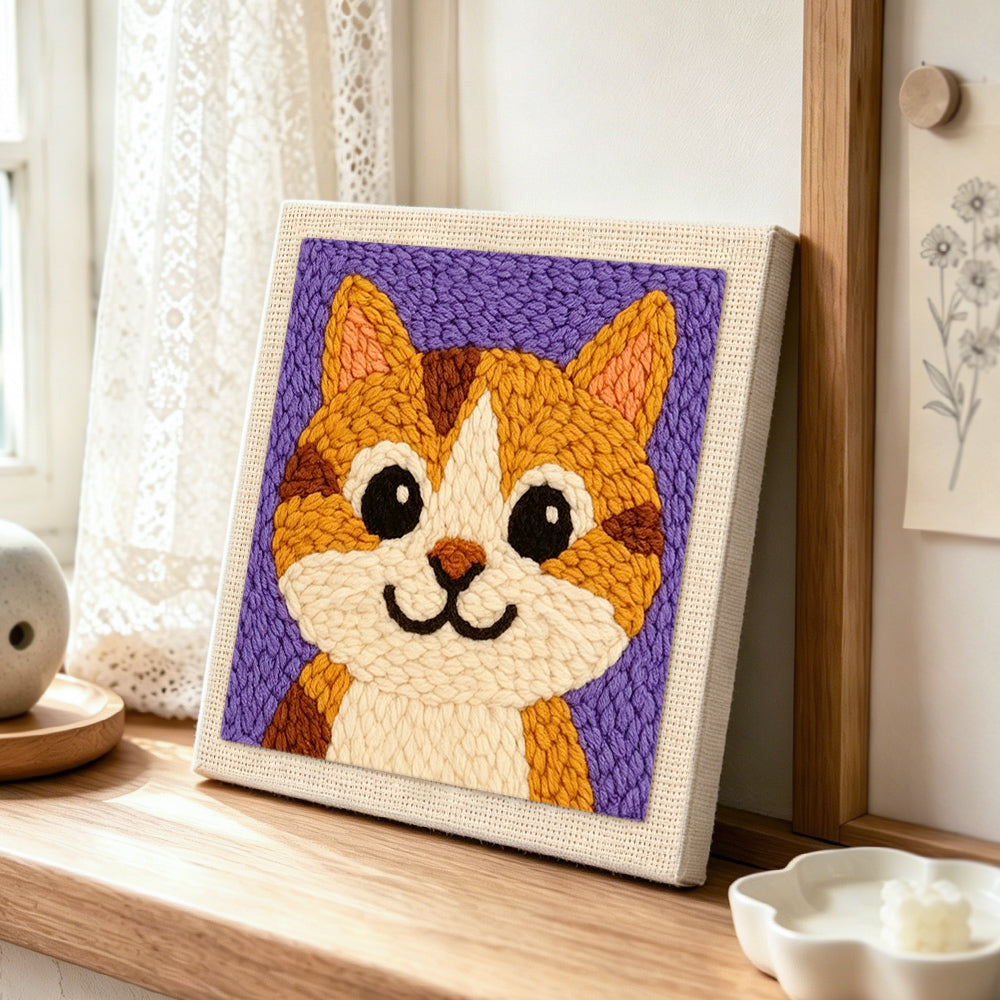 big-eyed orange tabby cat punch needle artwork displayed on a table