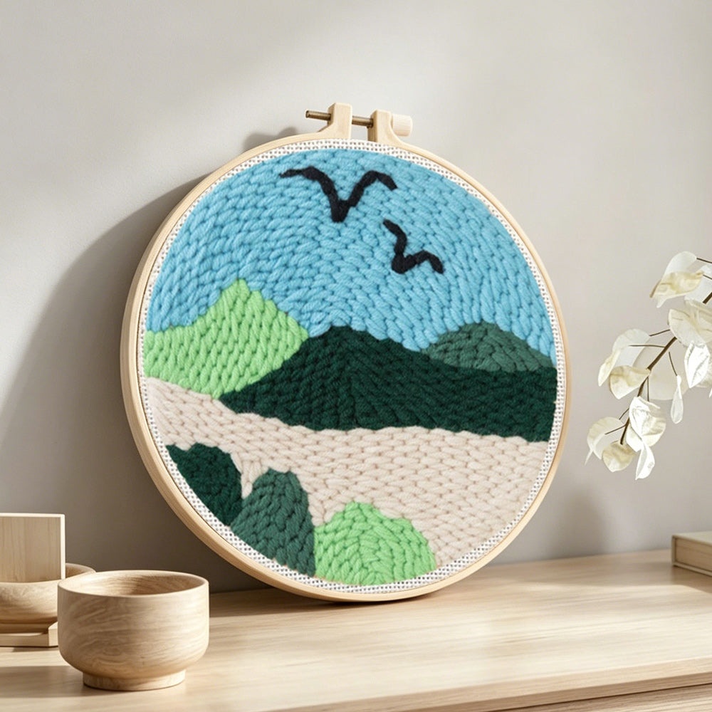 Birds over green mountain landscape punch needle artwork displayed on a table
