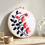 Black branches with pink and red blooms punch needle artwork displayed on a table