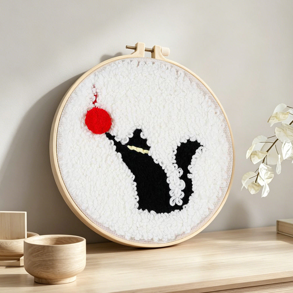 Black cat and red ball of yarn punch needle artwork displayed on a table