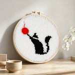 Black cat and red ball of yarn punch needle artwork displayed on a table