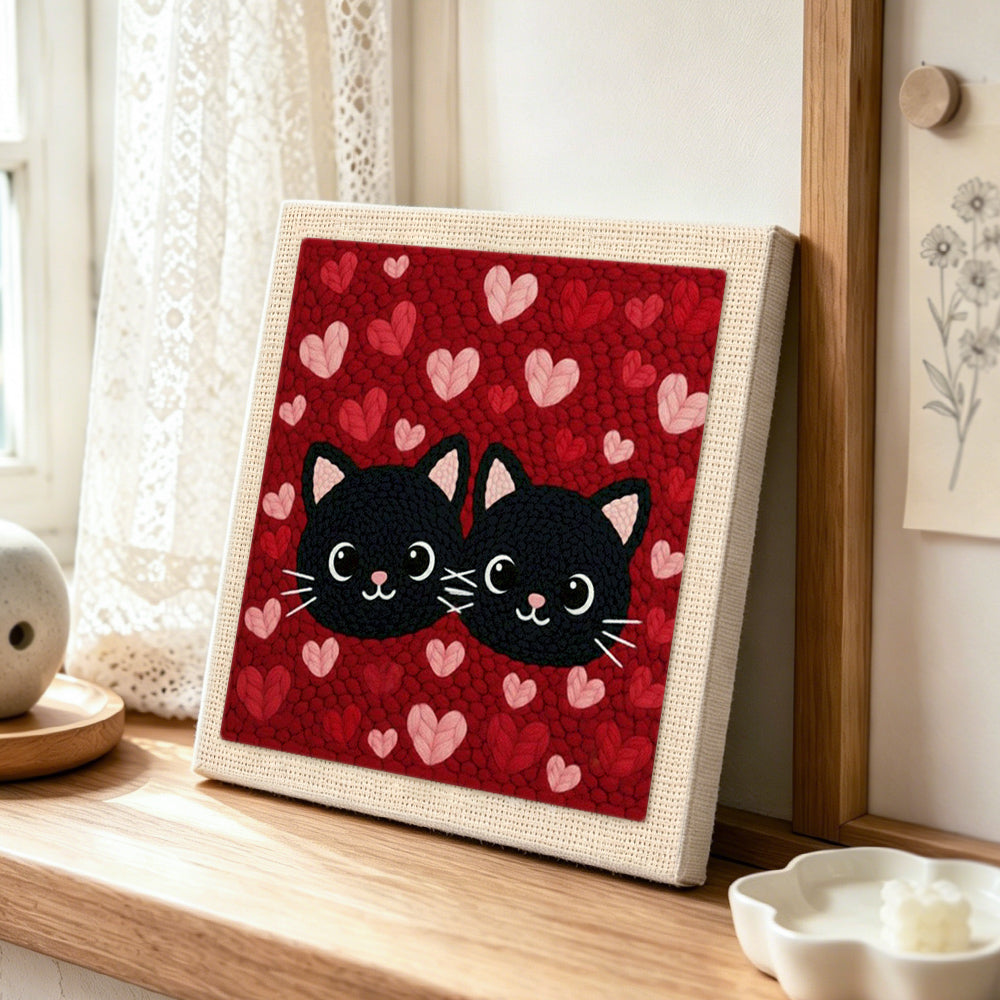 Black cat couple surrounded by hearts punch needle artwork displayed on a table