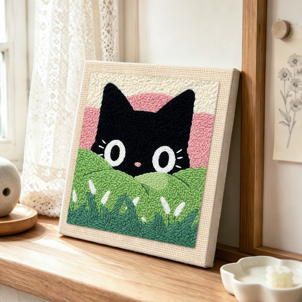 Black cat in green meadow punch needle artwork displayed on a table