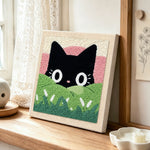 Black cat in green meadow punch needle artwork displayed on a table
