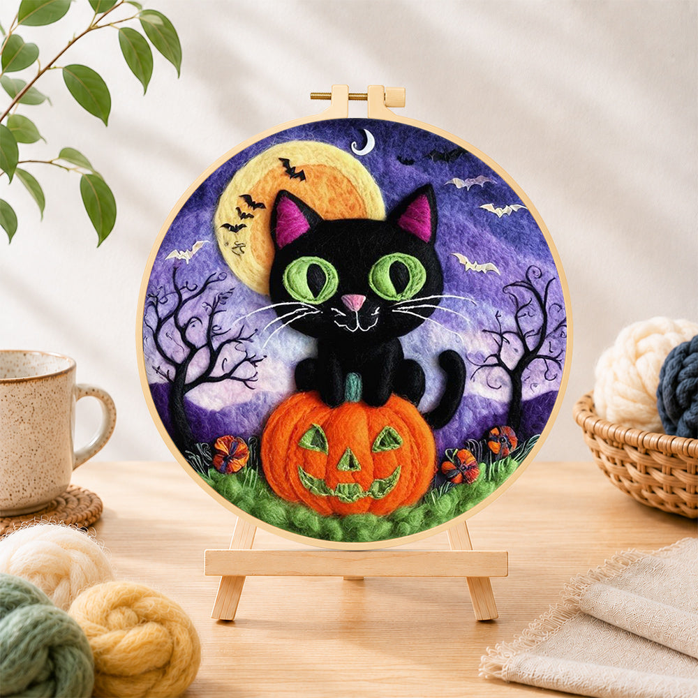 Finished black cat with green eyes on pumpkin needle felting displayed on a wooden easel