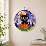 Black cat with green eyes on pumpkin needle felt wall art displayed in a bright home interior