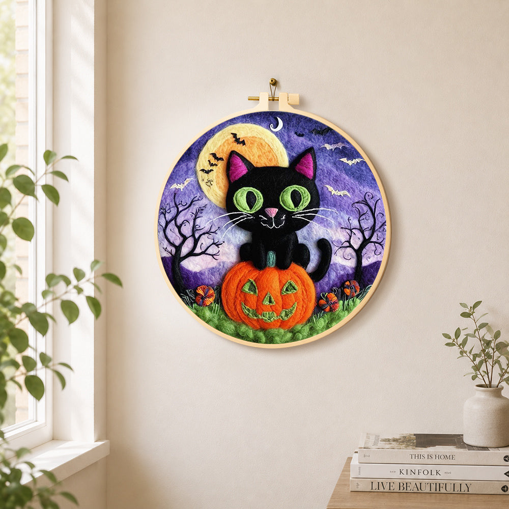 Black cat with green eyes on pumpkin needle felt wall art displayed in a bright home interior