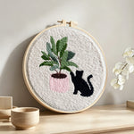 Black cat with houseplant punch needle artwork displayed on a table