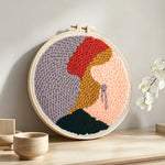 Blonde woman in red hat punch needle artwork displayed on a table