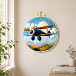 Blue biplane flying needle felt wall art displayed in a bright home interior
