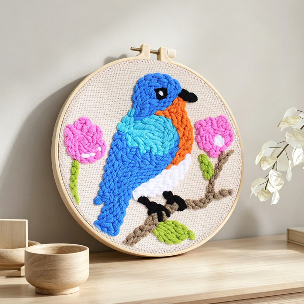 Blue bird and pink flowers punch needle artwork displayed on a table