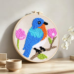 Blue bird and pink flowers punch needle artwork displayed on a table
