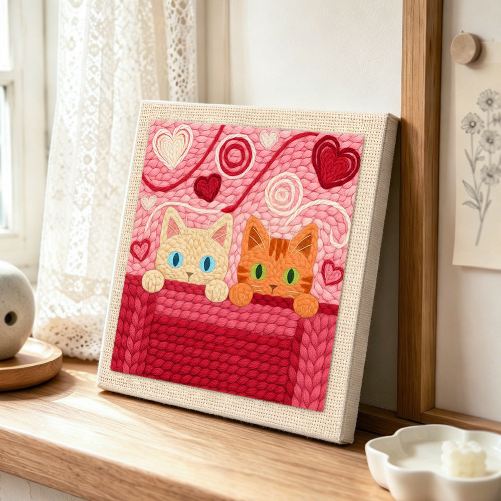 Blue-eyed and green-eyed cats peeking punch needle artwork displayed on a table
