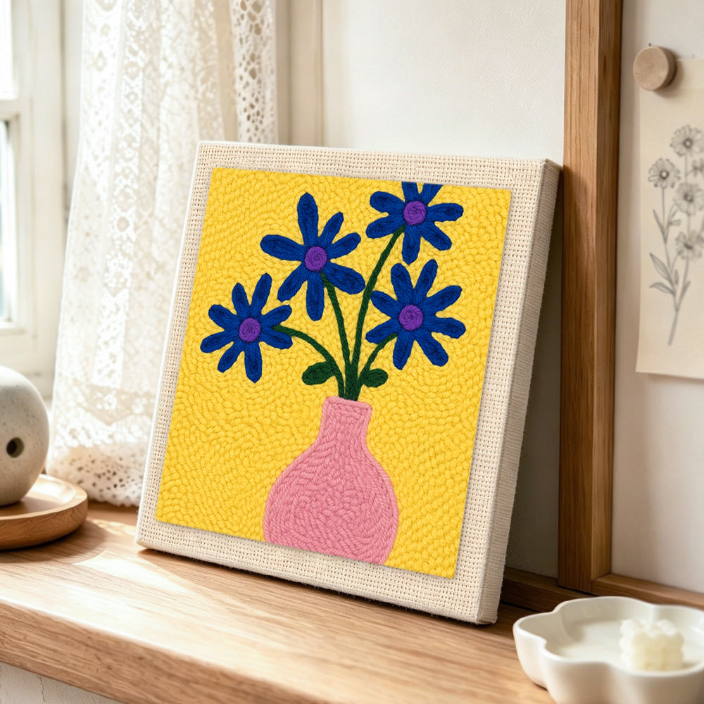 Blue flowers in a pink vase punch needle artwork displayed on a table