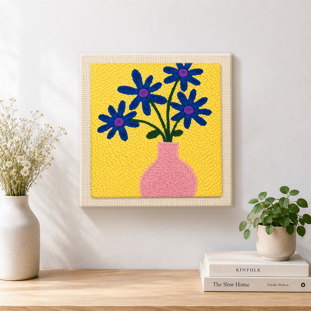 Finished blue flowers in a pink vase artwork displayed on a wall