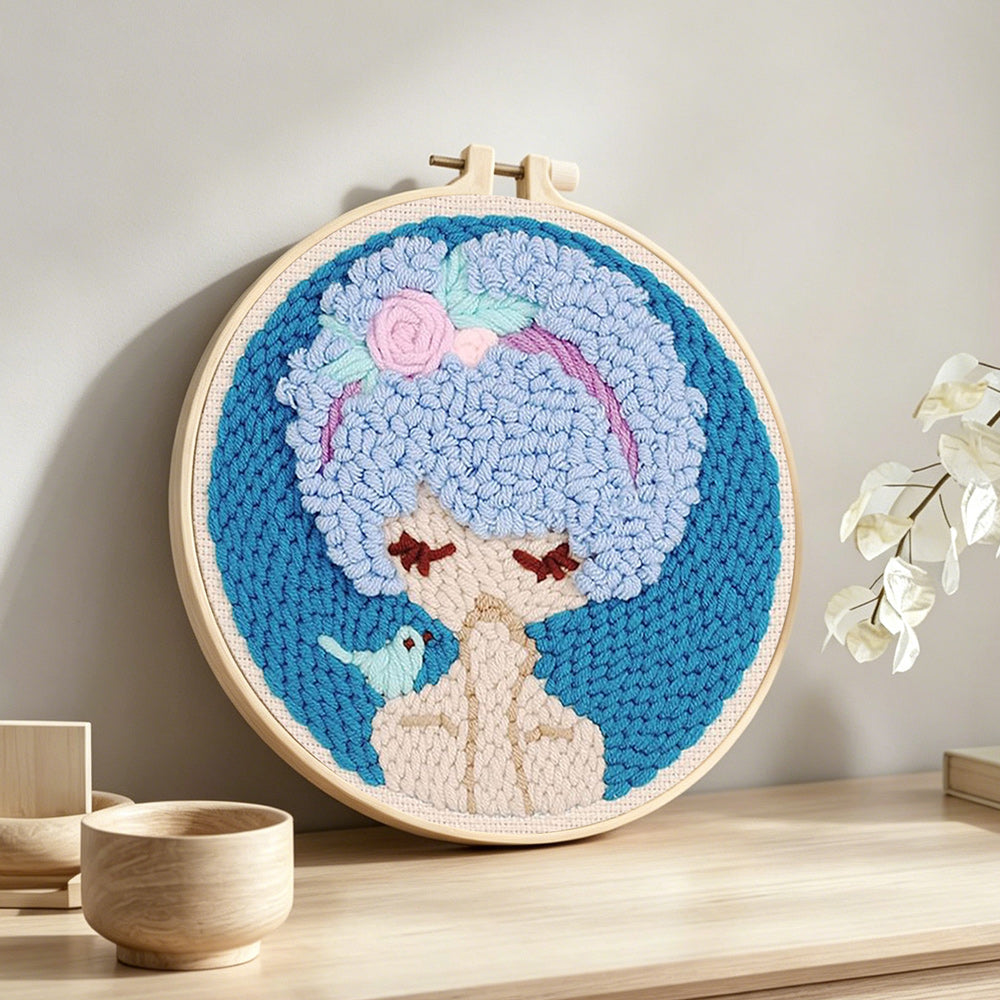 Blue haired girl with bird punch needle artwork displayed on a table