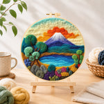 Finished blue lake, green trees and snow mountain needle felting displayed on a wooden easel