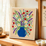 Blue vase with lavender, daisies and poppies punch needle artwork displayed on a table