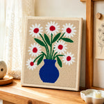 Blue vase with red-centred daisies punch needle artwork displayed on a table