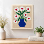 Finished blue vase with red-centred daisies artwork displayed on a wall