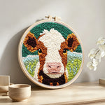 Brown and white cow face punch needle artwork displayed on a table