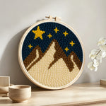 Brown and white snowy mountains under a starry sky punch needle artwork displayed on a table