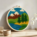 Brown mountains and pine trees by the river punch needle artwork displayed on a table