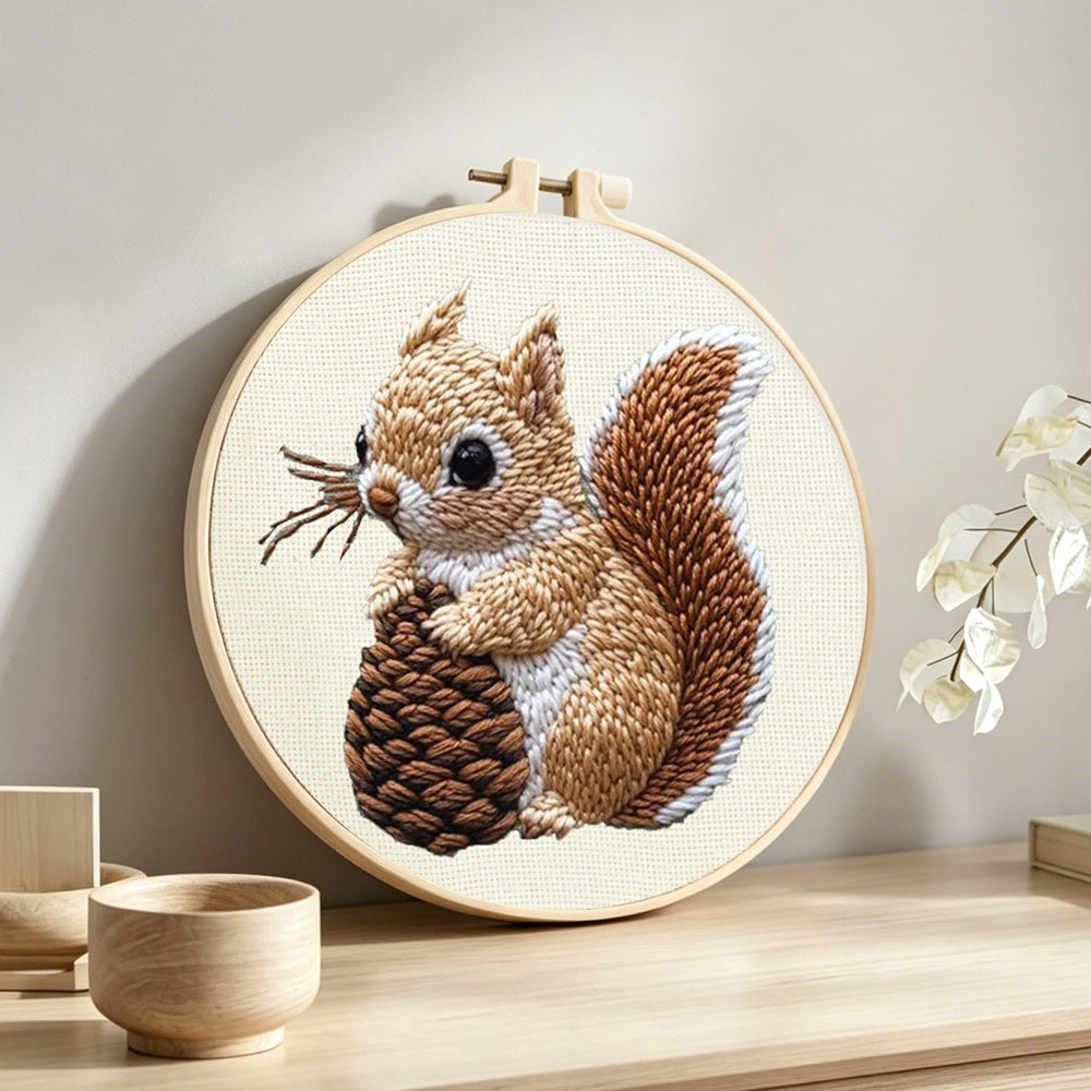 Brown squirrel holding pine cone punch needle artwork displayed on a table