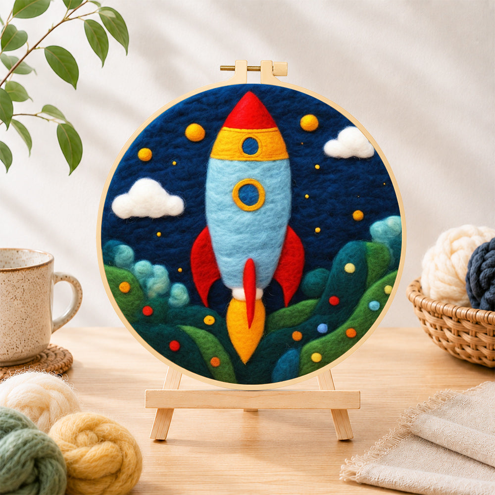 Finished cartoon rocket launch needle felting displayed on a wooden easel