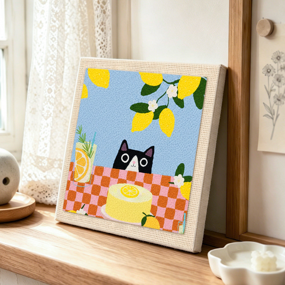 Cat peeking at lemon cake punch needle artwork displayed on a table