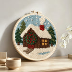 Christmas cabin with wreath and smoke punch needle artwork displayed on a table