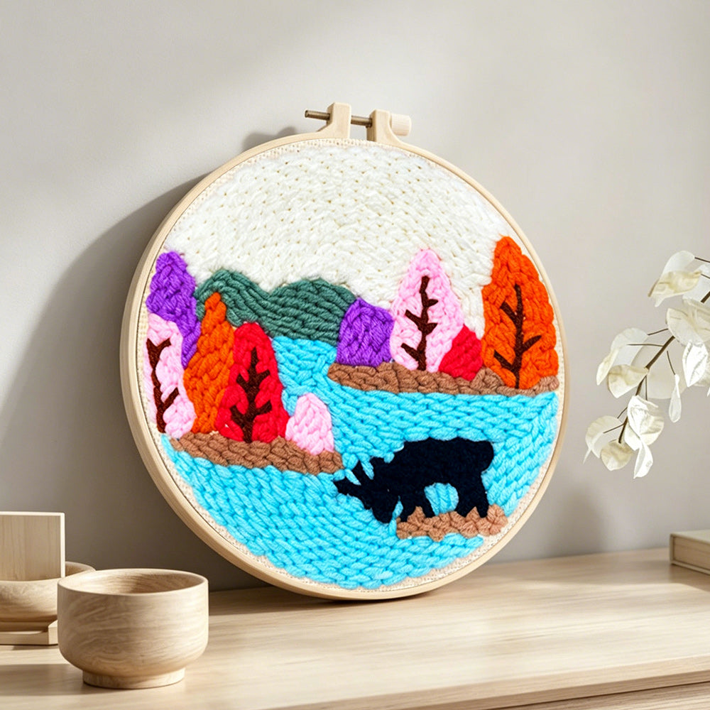 Colourful forest above a lake punch needle artwork displayed on a table