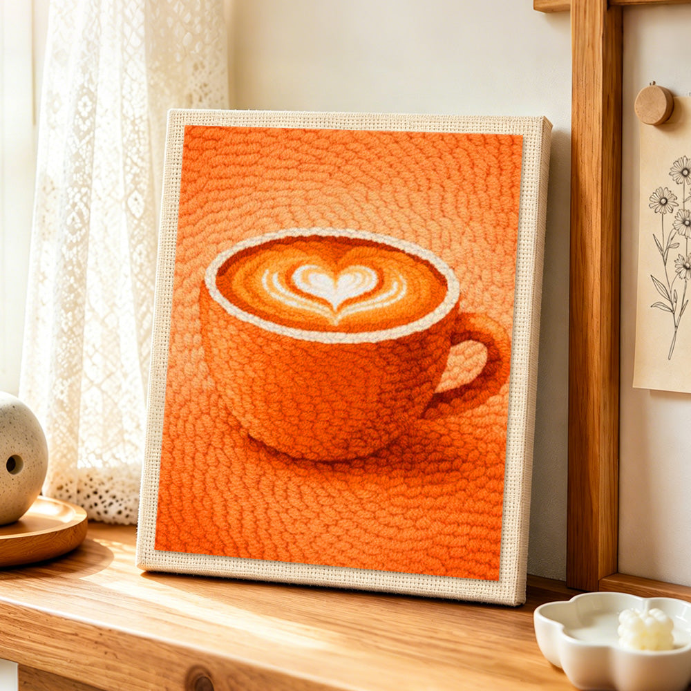 Cosy orange coffee cup with heart latte art punch needle artwork displayed on a table