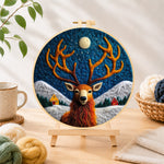 Finished cosy winter cabin and stag needle felting displayed on a wooden easel