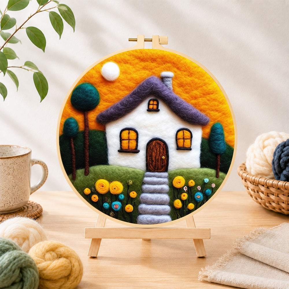 Finished cozy cottage and orange sunset needle felting displayed on a wooden easel