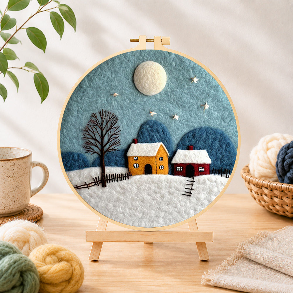 Finished cozy village on a snowy night needle felting displayed on a wooden easel