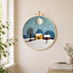 Cozy village on a snowy night needle felt wall art displayed in a bright home interior