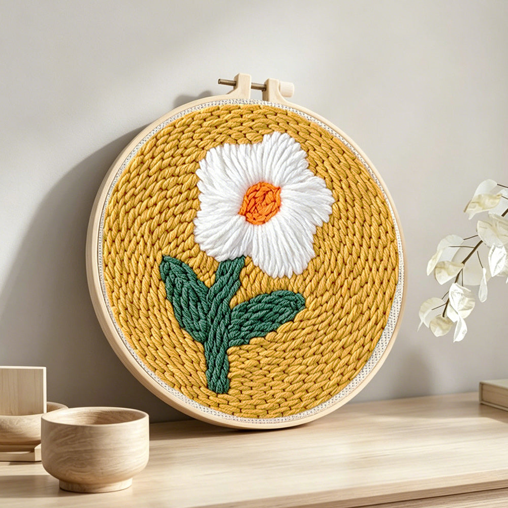 Cream flower on mustard yellow punch needle artwork displayed on a table