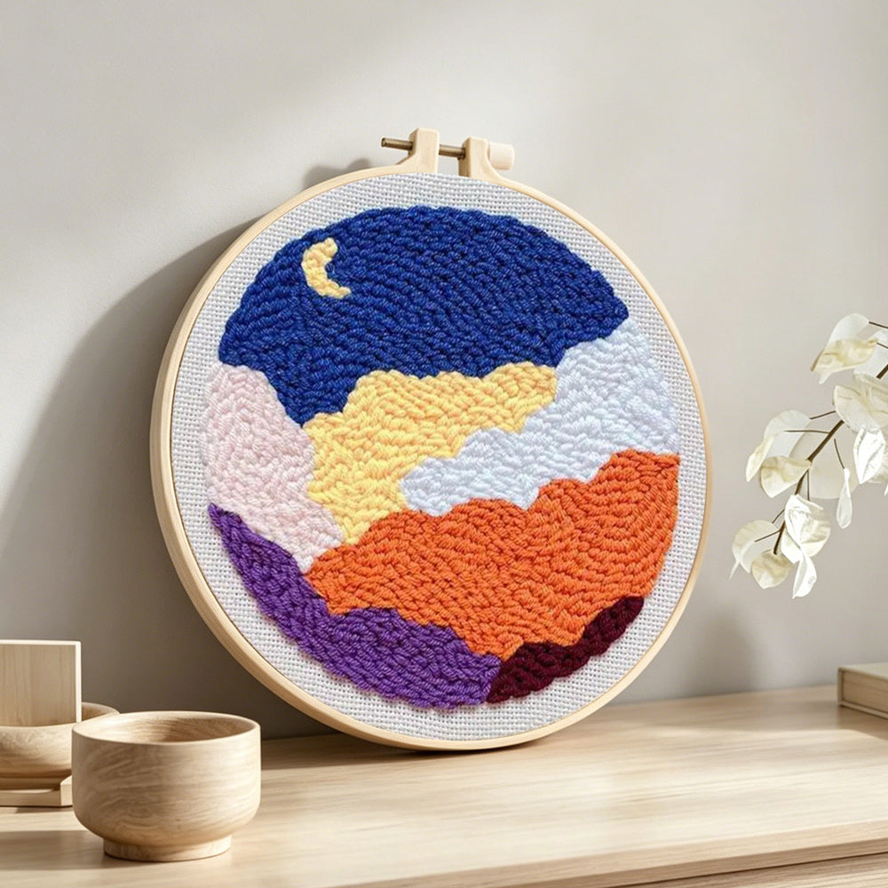 Crescent moon and colourful layered clouds punch needle artwork displayed on a table