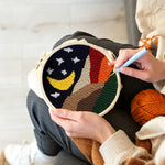 Creating handmade crescent moon and white stars above the colourful mountains punch needle artwork