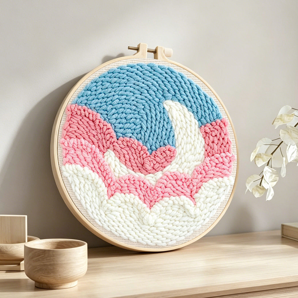 Crescent moon over pink and white clouds punch needle artwork displayed on a table