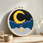 Crescent moon, sea and mountains punch needle artwork displayed on a table