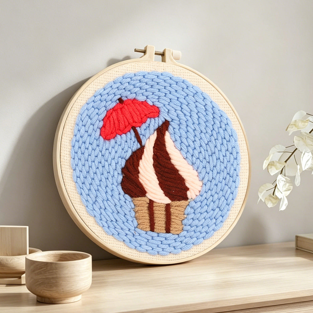 Cupcake with red umbrella punch needle artwork displayed on a table